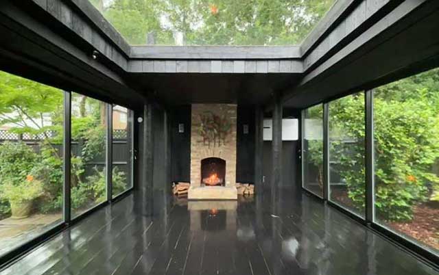 A roaring fire at the end of the empty pavilion, with greenery peeking through the glass roof, and outside the glass doors on either side.